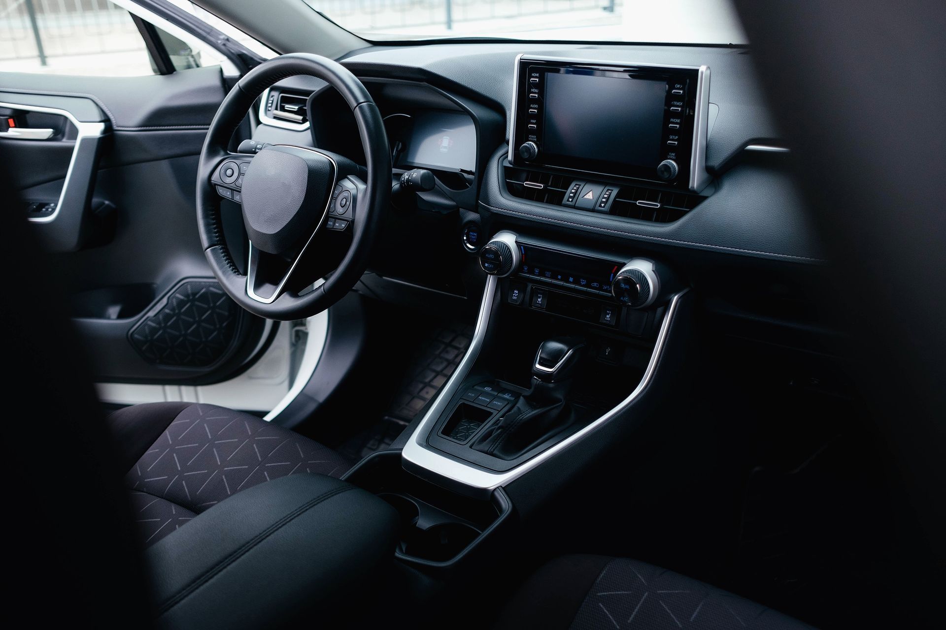 Interior view of a modern car: black dashboard, steering wheel, digital display, and center console with gear shift.
