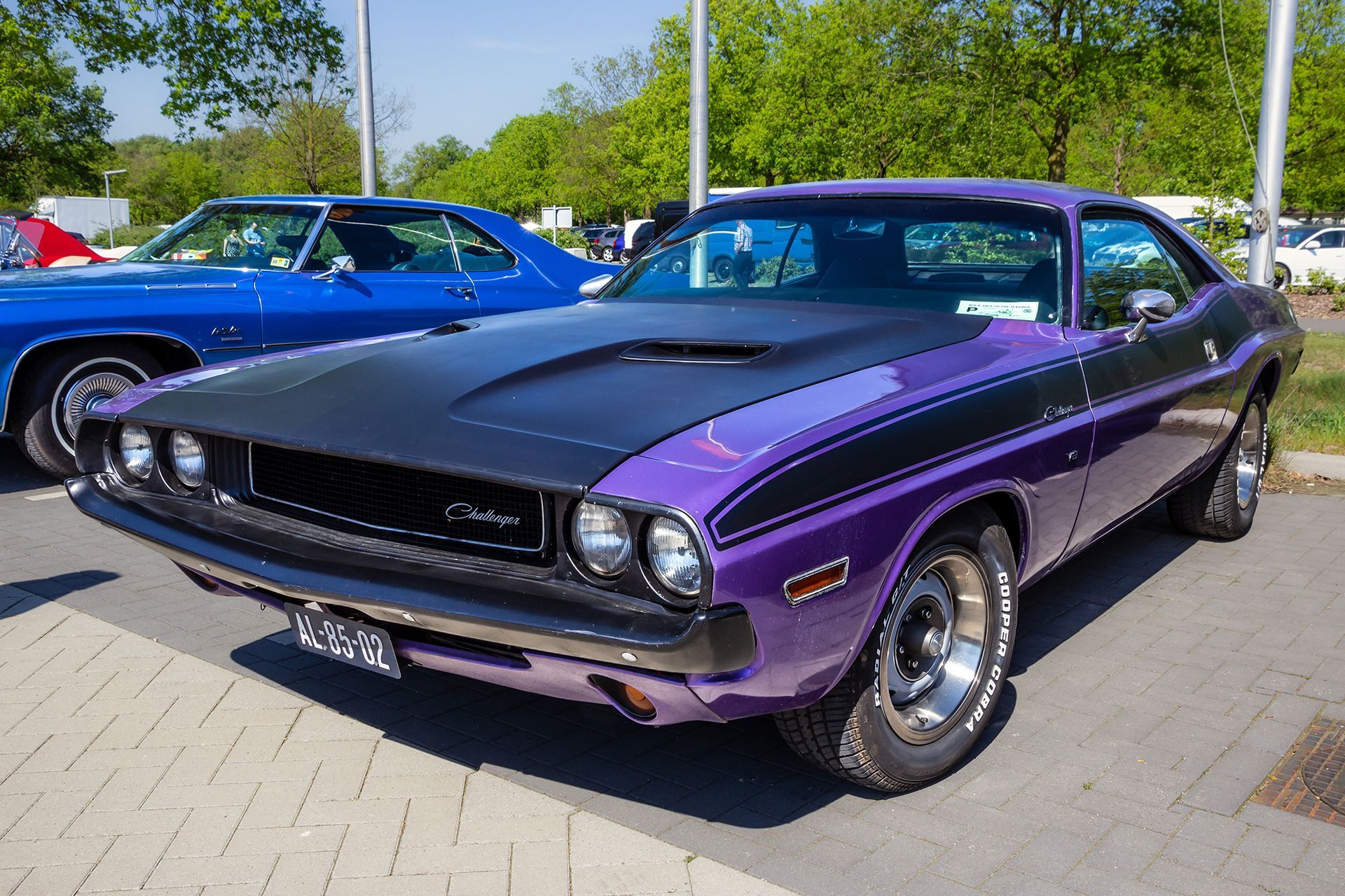 Purple 1970 Dodge Challenger with black hood and stripe at a car show.