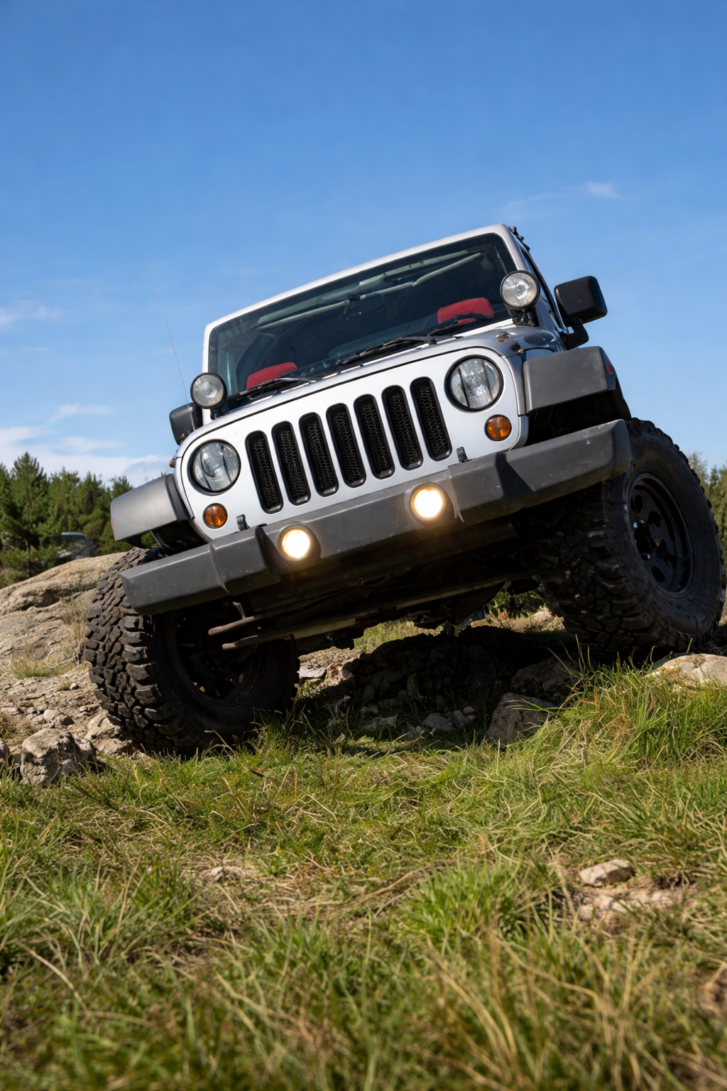 Silver Jeep Wrangler off-roading on a grassy hill, front wheels angled.