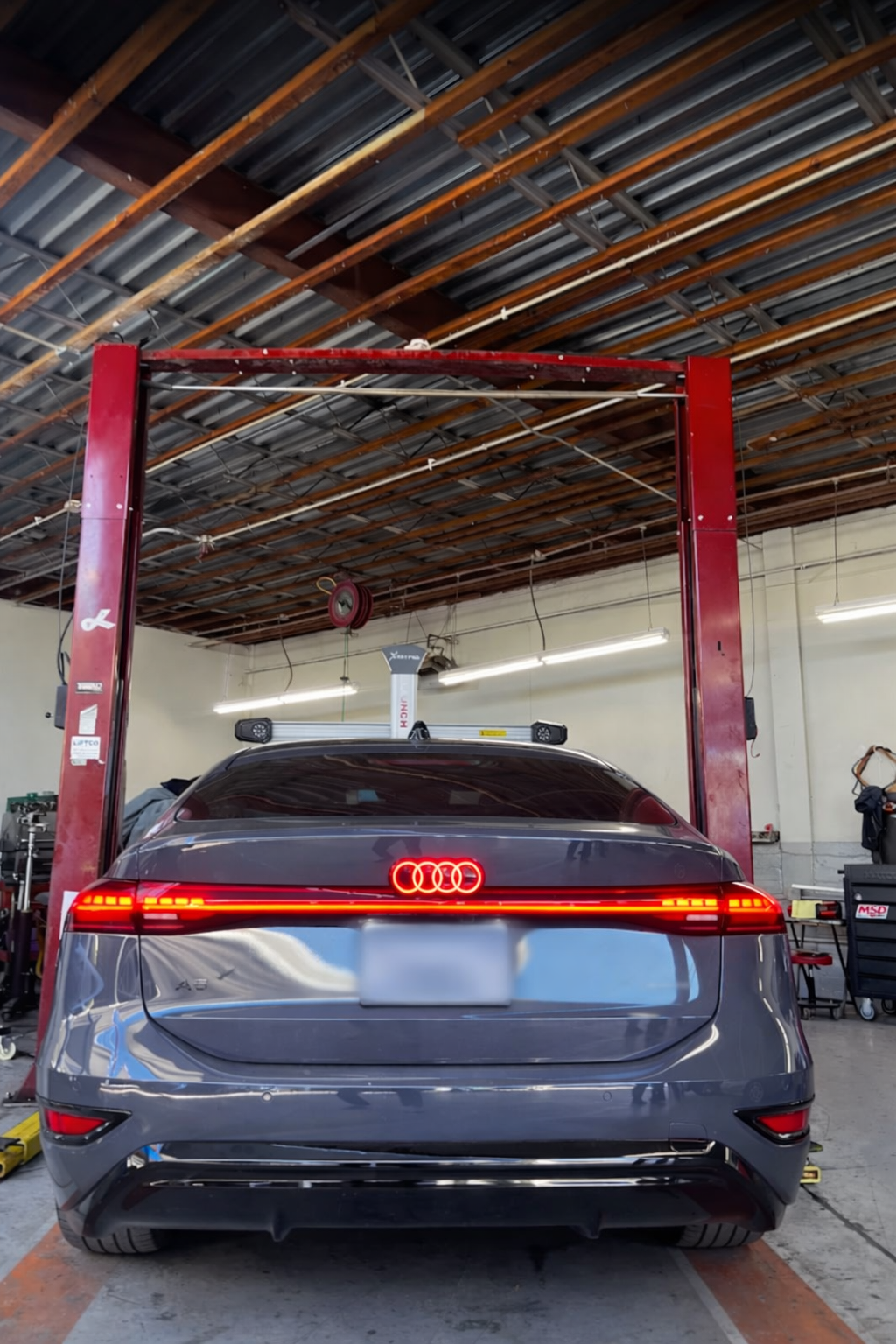 Gray Audi sedan inside a garage on a car lift; red tail lights on.