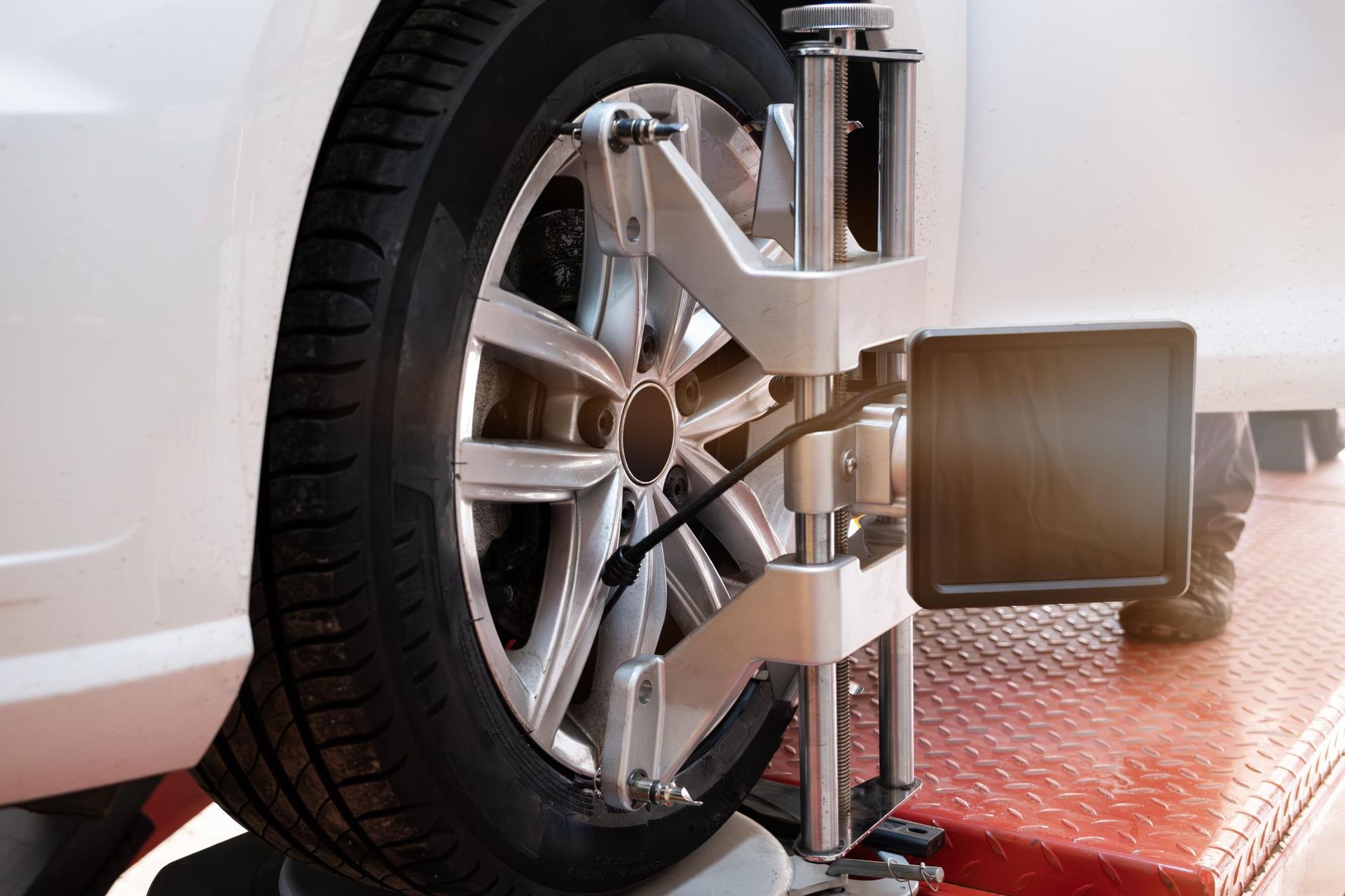 Car tire undergoing wheel alignment on a lift with attached sensors; silver, red, and black.