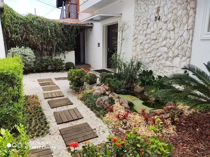 Um caminho de tábuas de madeira leva à entrada da casa. Paisagismo com plantas e pedras.