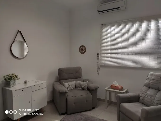 Sala de terapia aconchegante, em tons neutros, com poltronas reclináveis, uma pequena mesa, um espelho redondo e uma janela.