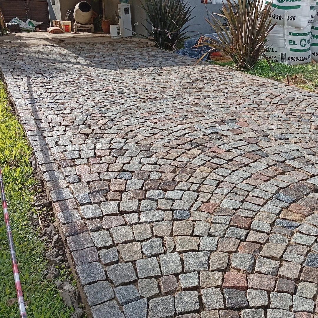 Camino de entrada adoquinado en diferentes tonos de gris, con un patrón curvo, bordeado de césped.