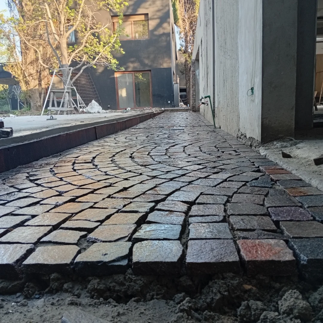 Adoquines de piedra semicirculares recién colocados en un camino. Obra con un edificio a la derecha.