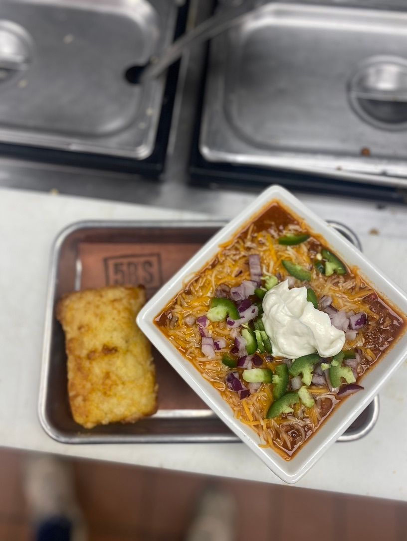 A bowl of chili next to a piece of cornbread
