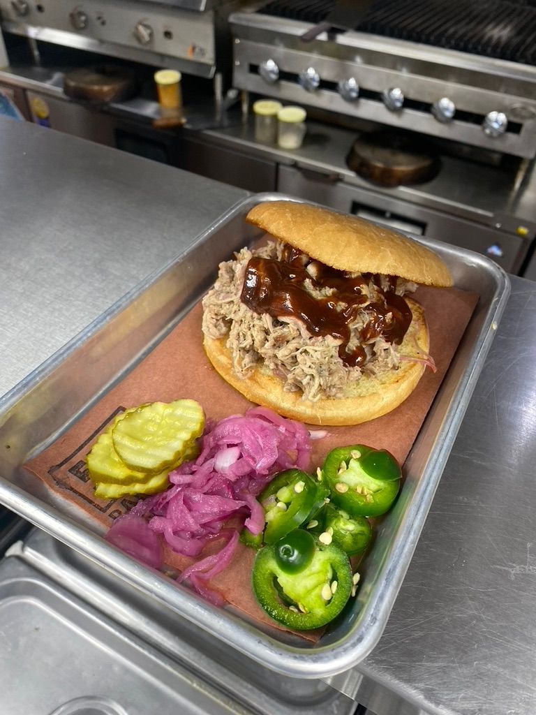A pulled pork sandwich with pickles , onions and jalapenos on a tray.