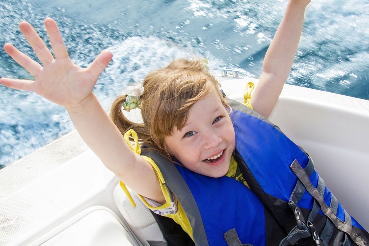 A little girl wearing a life jacket is sitting on a boat.