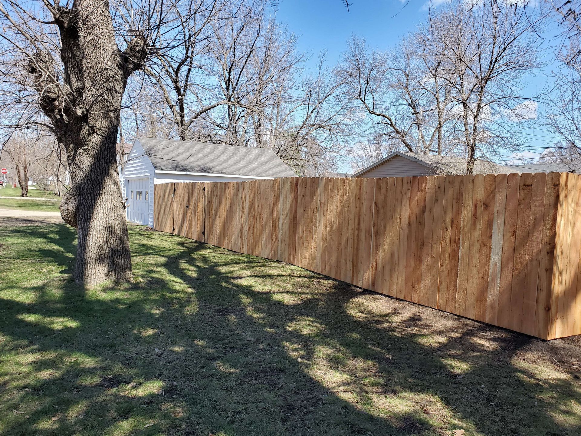 A wooden fence is surrounded by grass and trees in a yard.