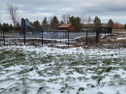 A snowy field with a fence and a shed in the background