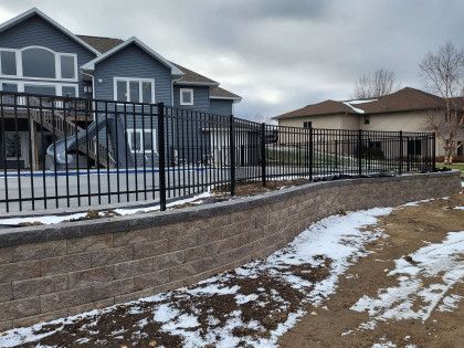 A fence surrounds a swimming pool in front of a house.