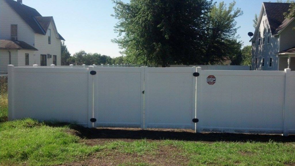 A white fence with a gate in the middle of a grassy field.