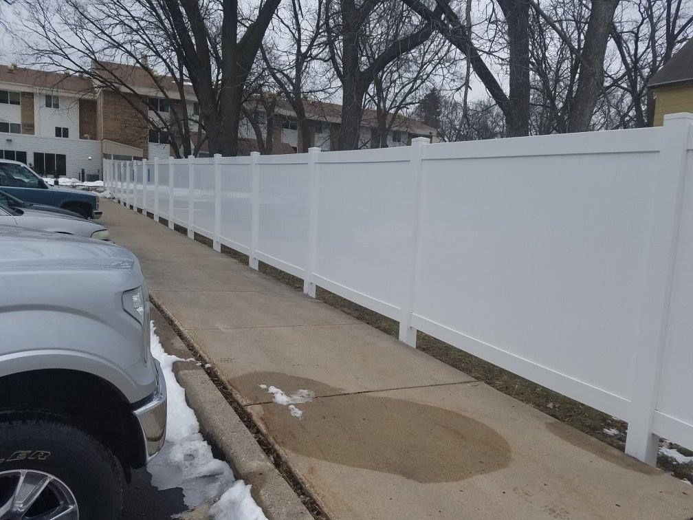 A white truck is parked on the side of the road next to a white fence.