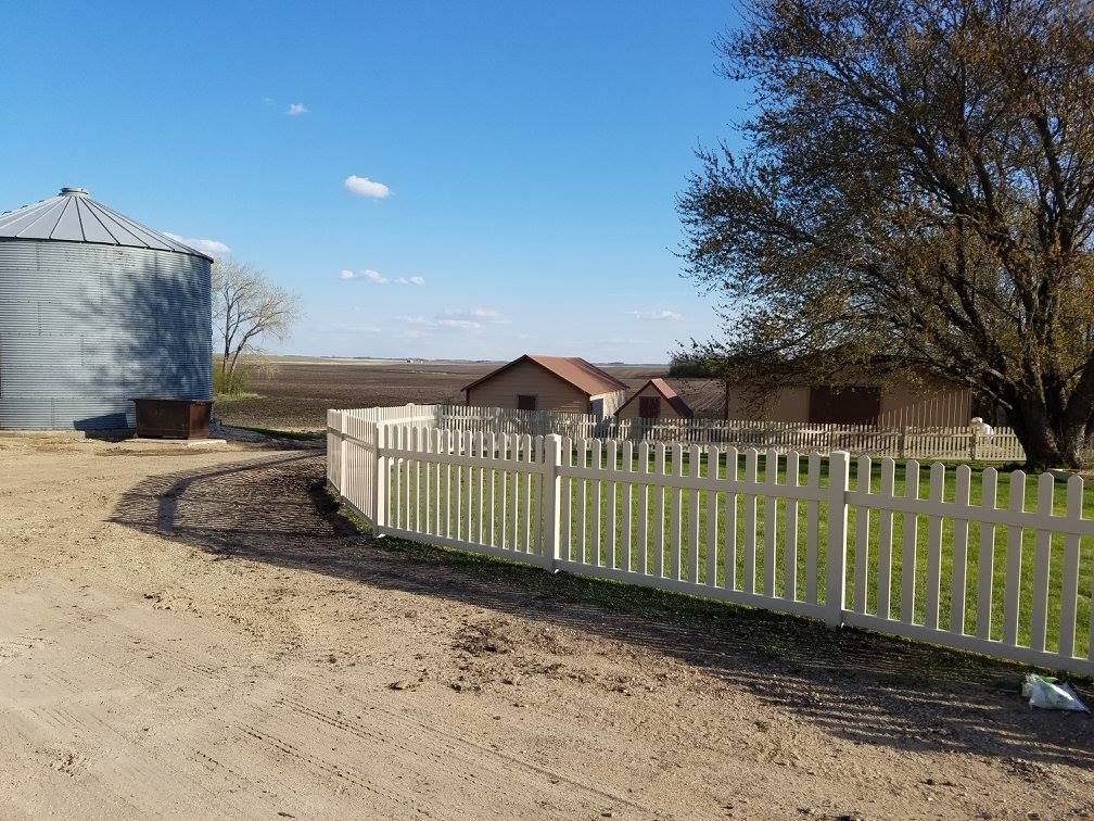 A white picket fence surrounds a farm with a silo in the background.