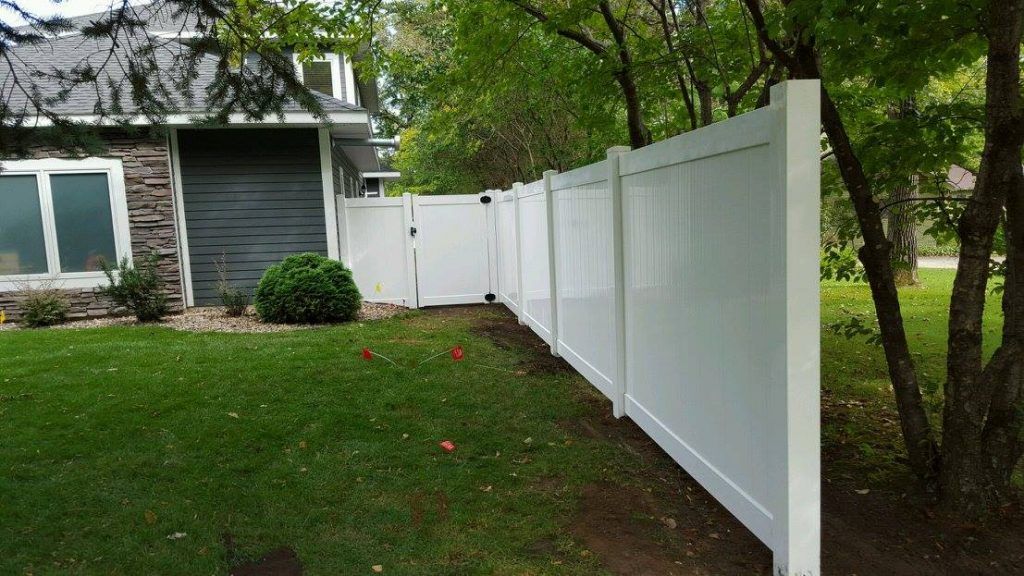 A white fence surrounds a lush green yard in front of a house.