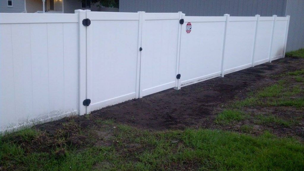 A white fence with a gate in the backyard of a house.