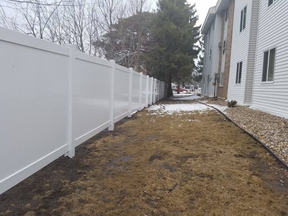 A white fence surrounds a grassy area next to a building.