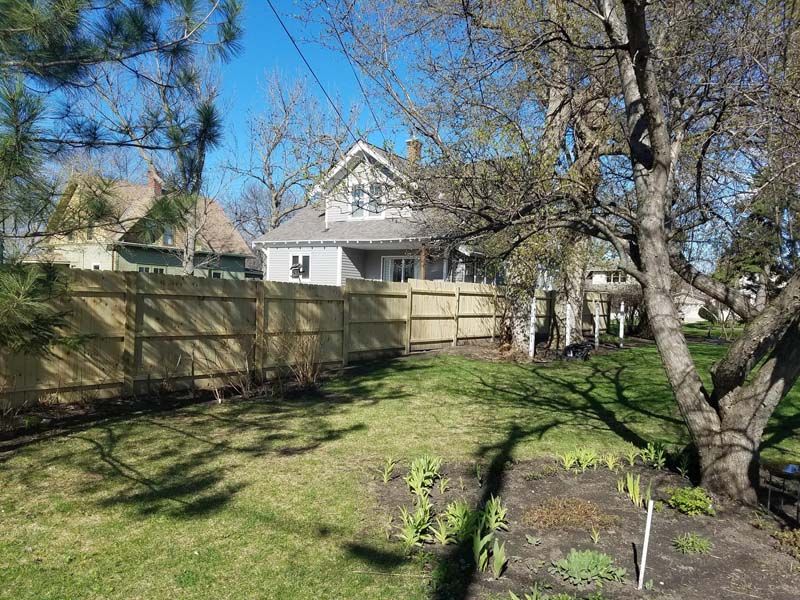 A backyard with a wooden fence and a house in the background.