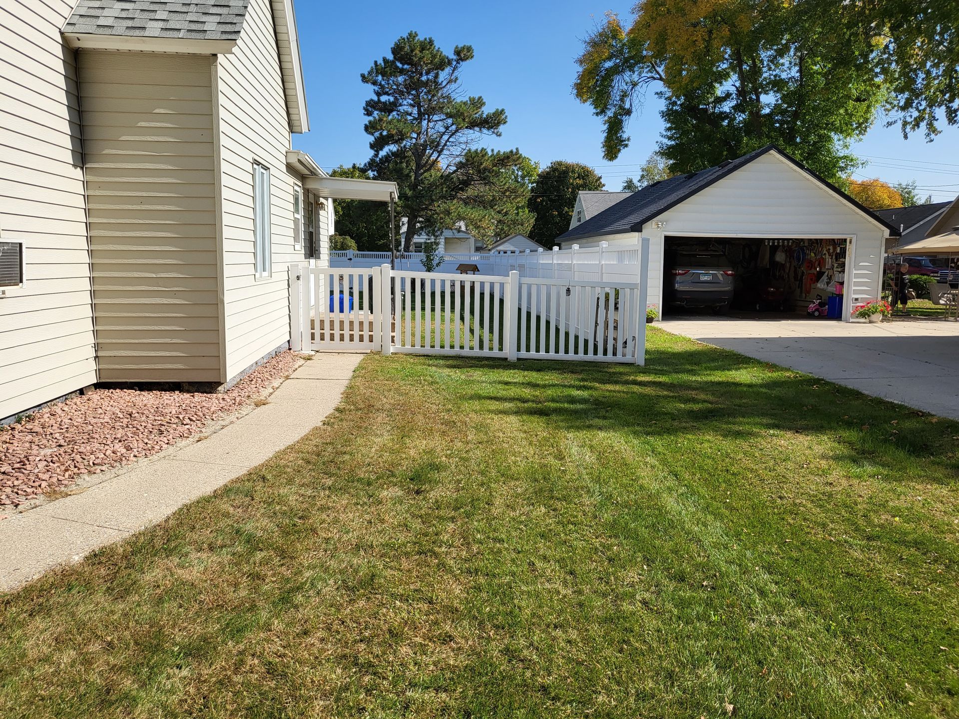 A white fence surrounds a lush green yard in front of a house.