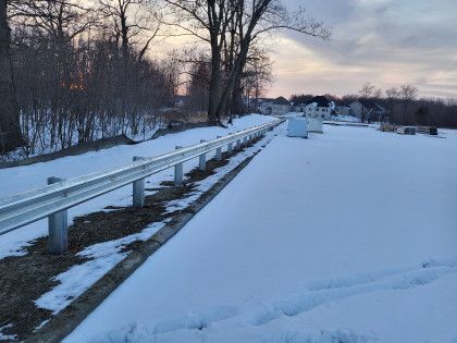 A snowy road with a railing and trees in the background