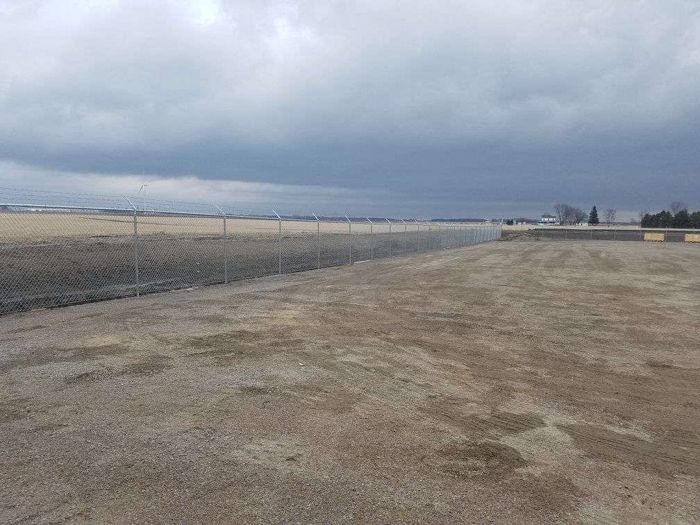 A fence surrounds a dirt field with a cloudy sky in the background.