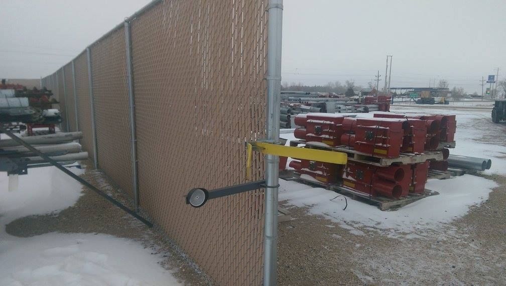 A chain link fence is sitting in the snow next to a pile of pallets.