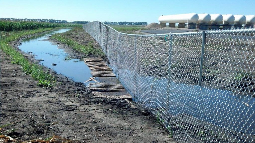A chain link fence surrounds a muddy stream in a field.