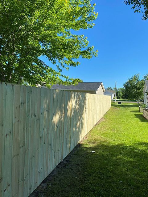 A wooden fence surrounds a lush green yard with a house in the background.