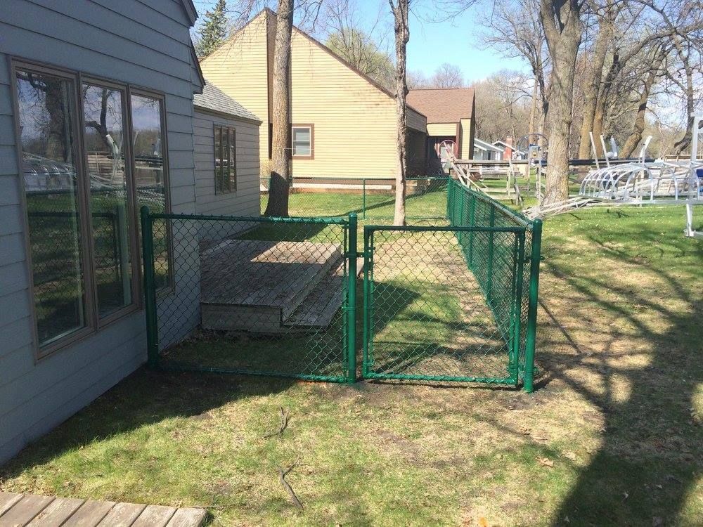 A chain link fence with a gate in the backyard of a house.