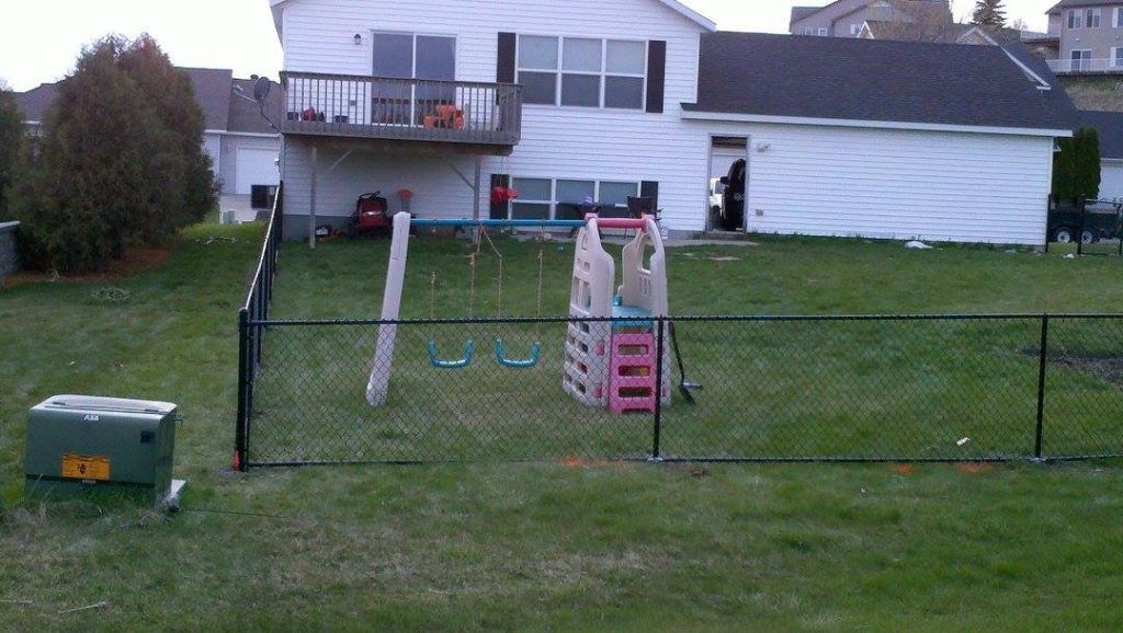 A backyard with a fence and a house in the background