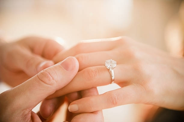 Woman's hand with engagement ring held by man, close-up, romantic proposal, engagement jewelry.