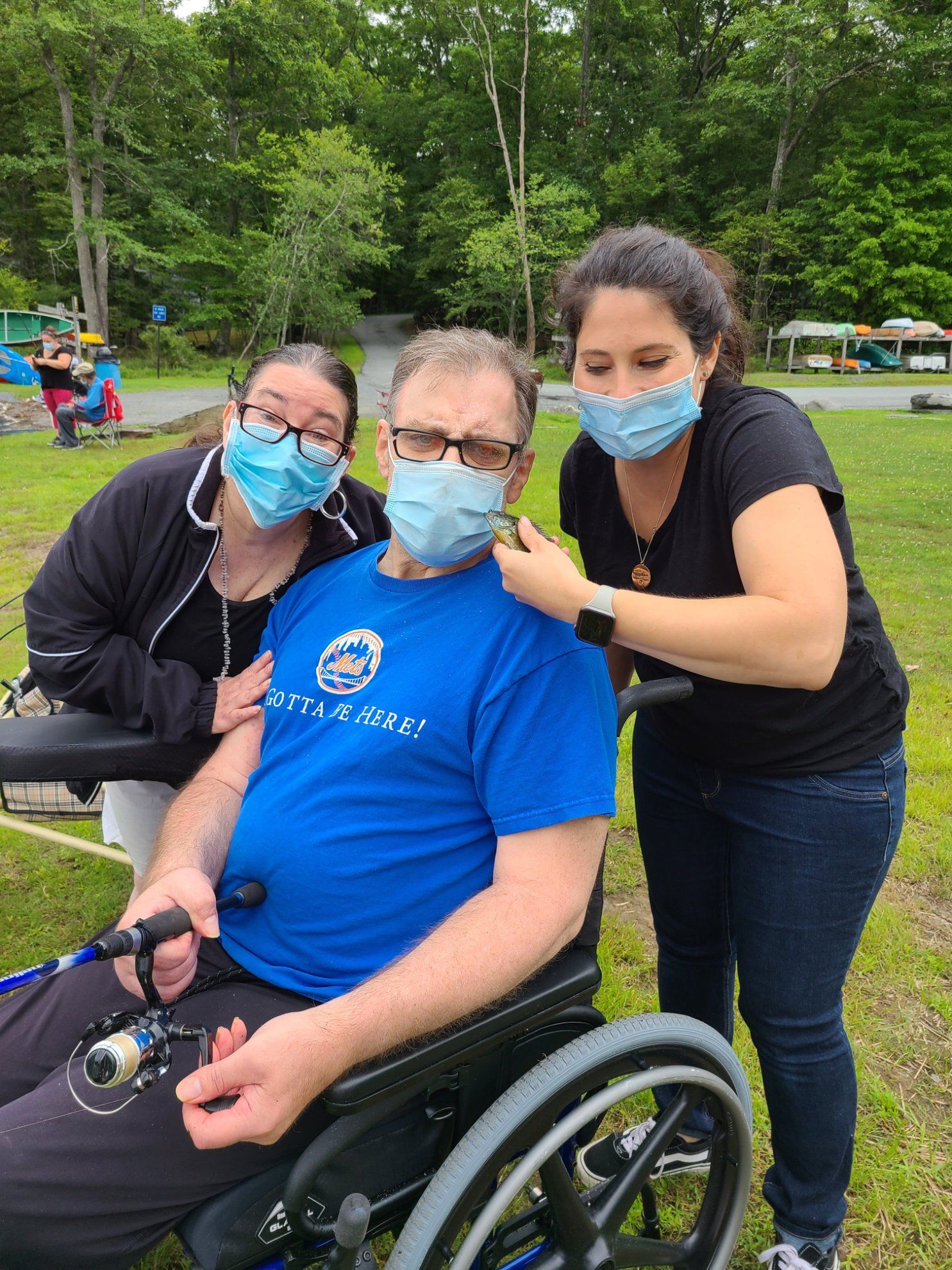 A man in a wheelchair is being helped by two women wearing face masks.