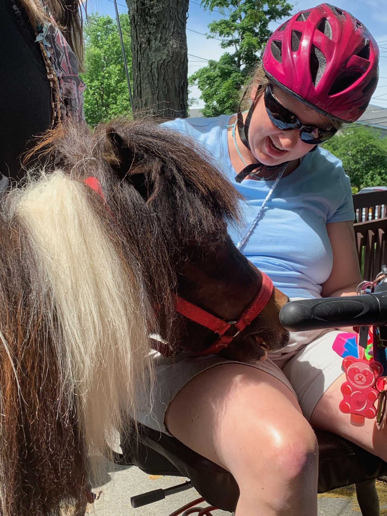 A woman wearing a pink helmet is sitting next to a pony.