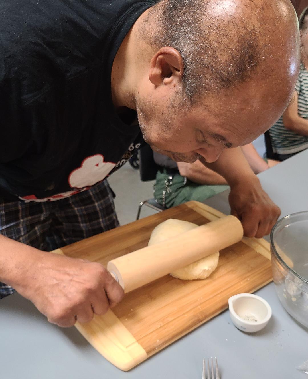 A man in a black shirt is rolling dough on a cutting board