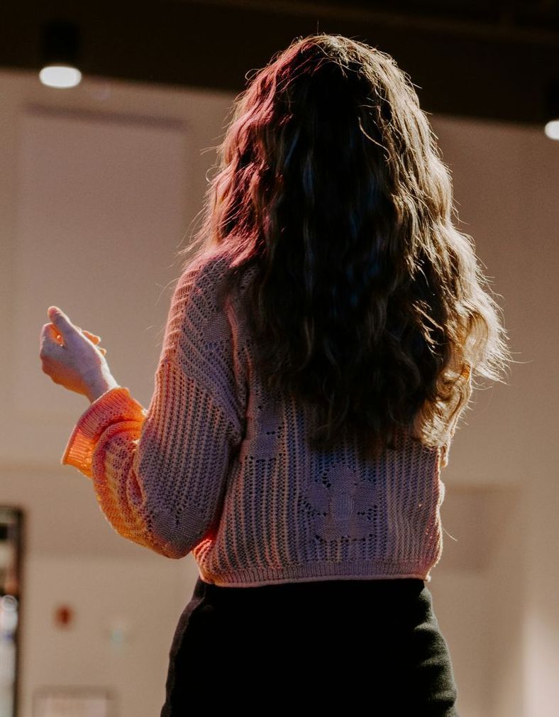 A woman with long hair is standing in a room with her back to the camera.