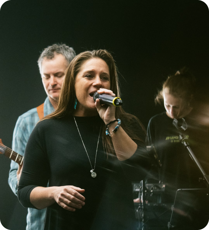 A woman singing into a microphone with a man playing a guitar in the background