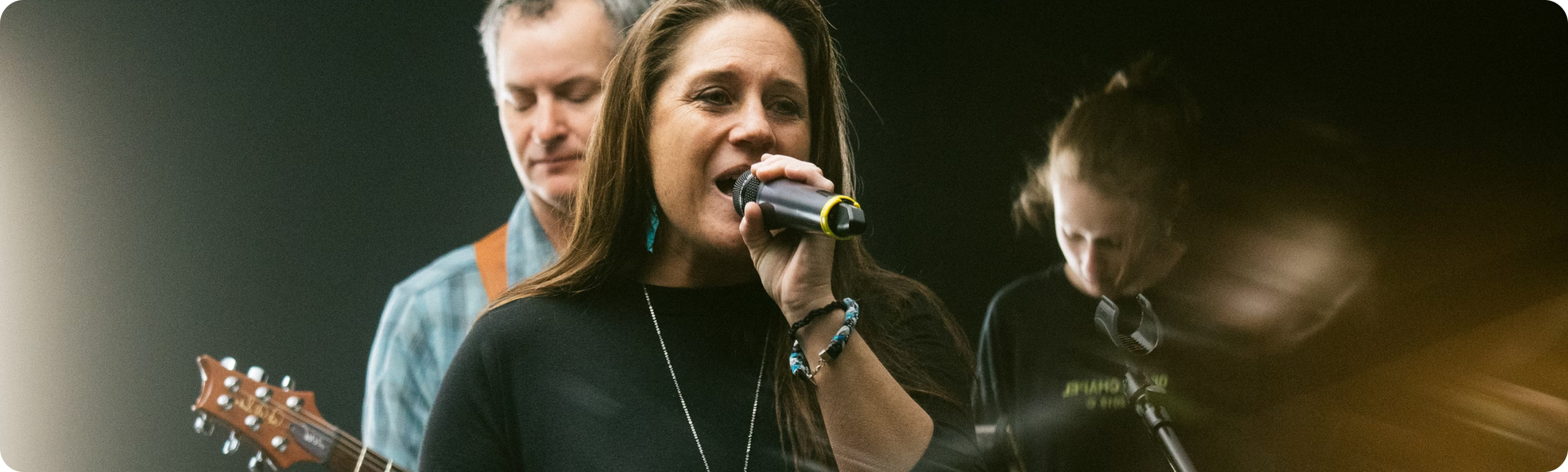 A woman is singing into a microphone while a man plays a guitar.