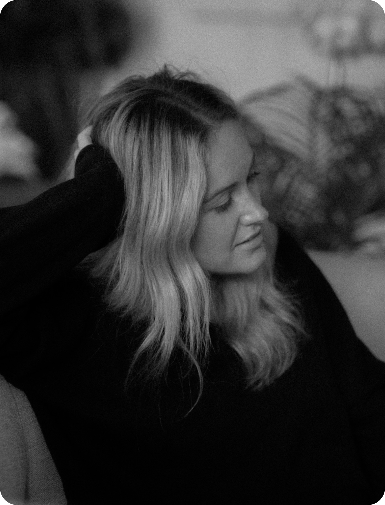 A black and white photo of a woman sitting on a couch with her hand in her hair.