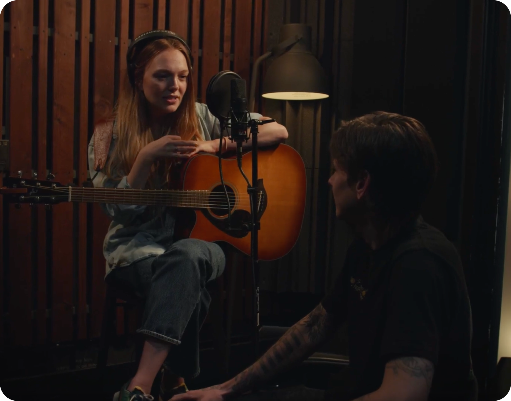 A woman is playing a guitar next to a man in front of a microphone.