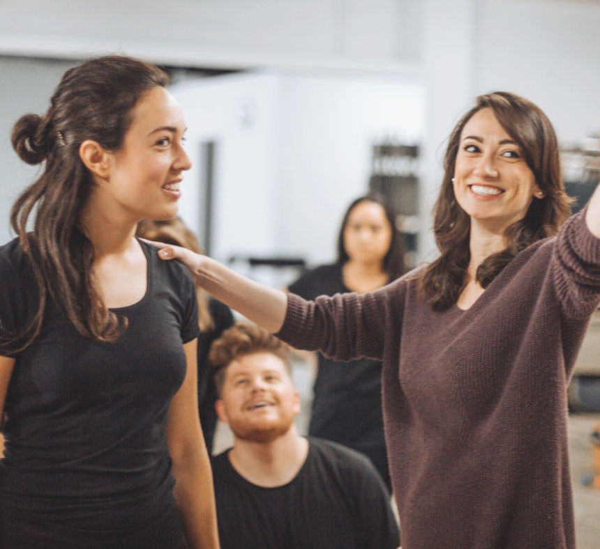 A woman in a purple sweater is pointing at another woman in a black shirt