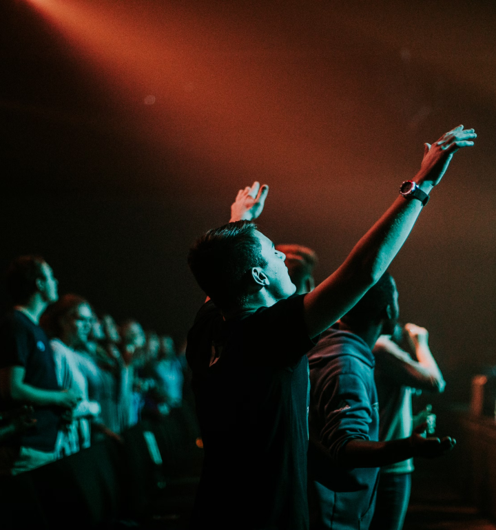 A group of people are standing in a dark room with their hands in the air.