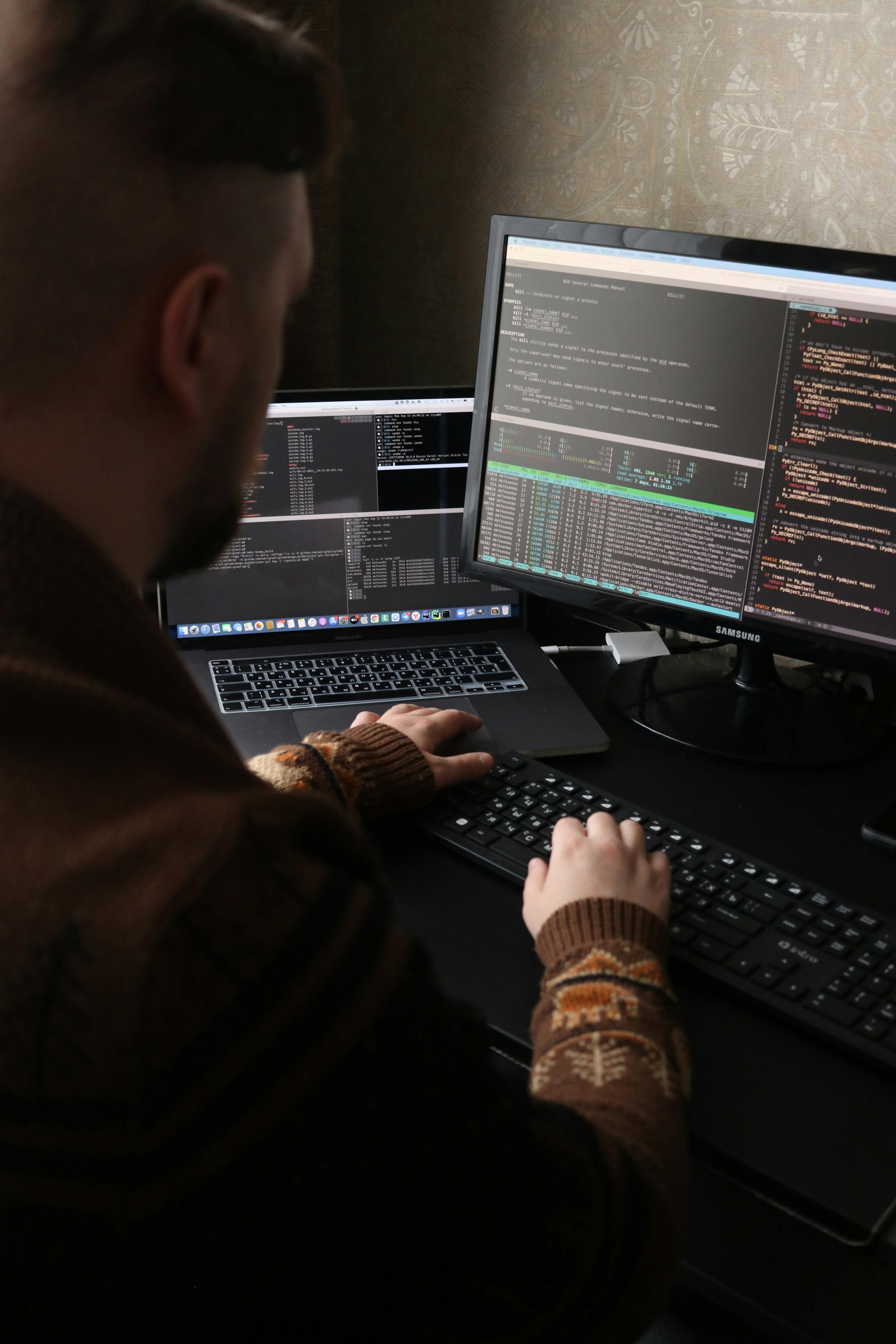 A man is typing on a keyboard in front of two computer monitors.