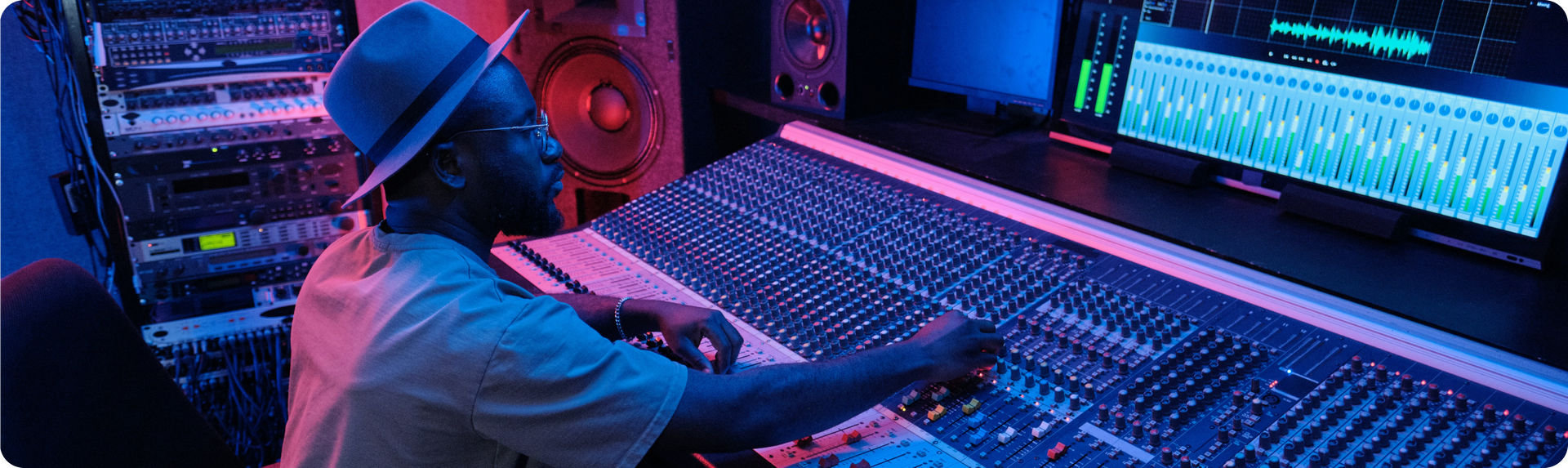 A man in a hat is sitting at a mixer in a recording studio.