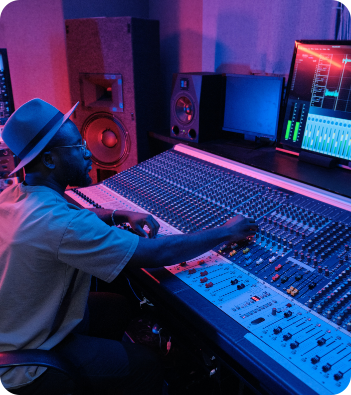 A man in a hat is sitting at a mixer in a recording studio