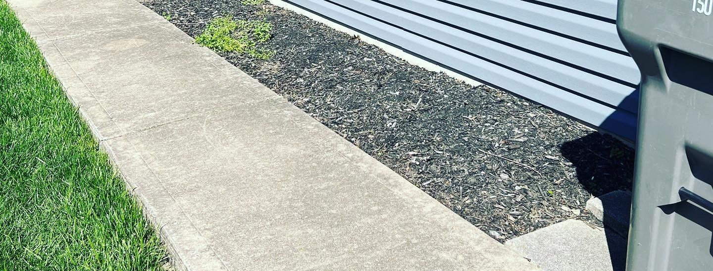 A trash can is sitting on the sidewalk next to a house.