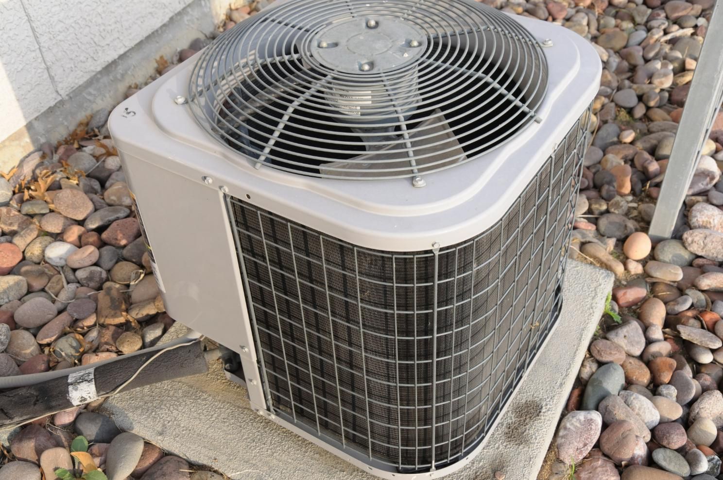 Outdoor air conditioning unit with fan and coils, on a concrete base with rocks.
