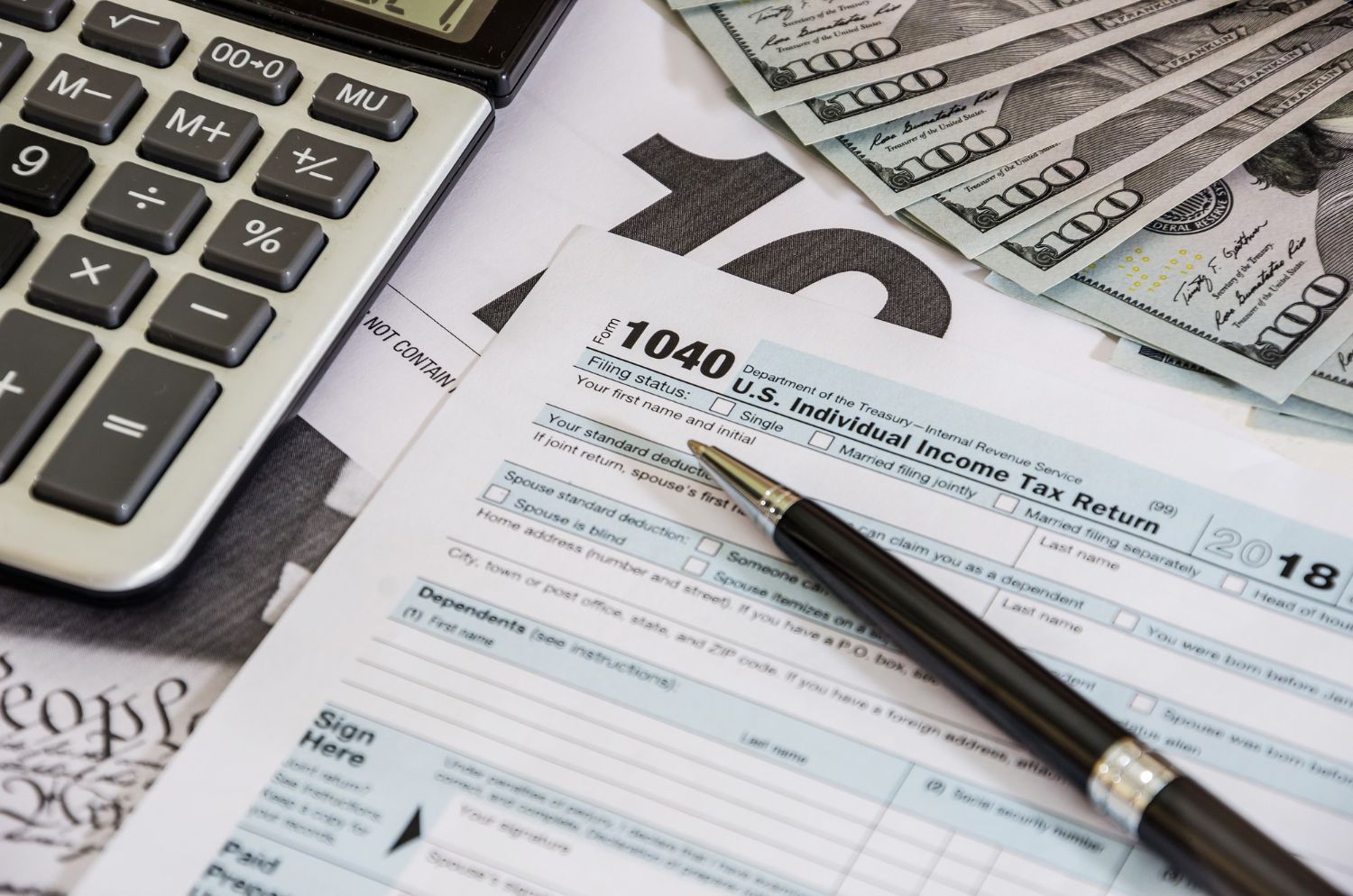 Calculator, tax form (1040), pen, and money on a white surface.