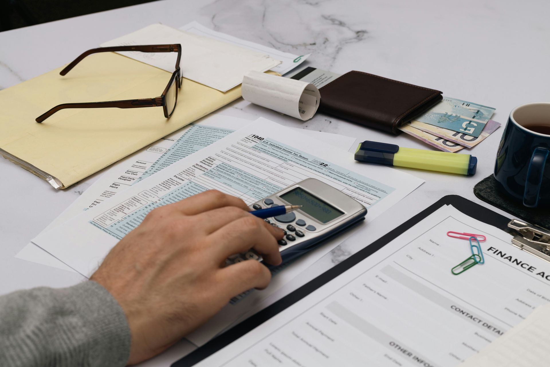 Person using a calculator on a desk with financial documents, glasses, and a wallet.