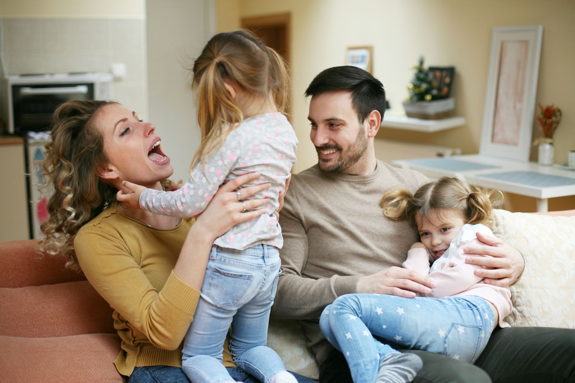 Family of four, two young children, on a sofa, laughing and interacting.