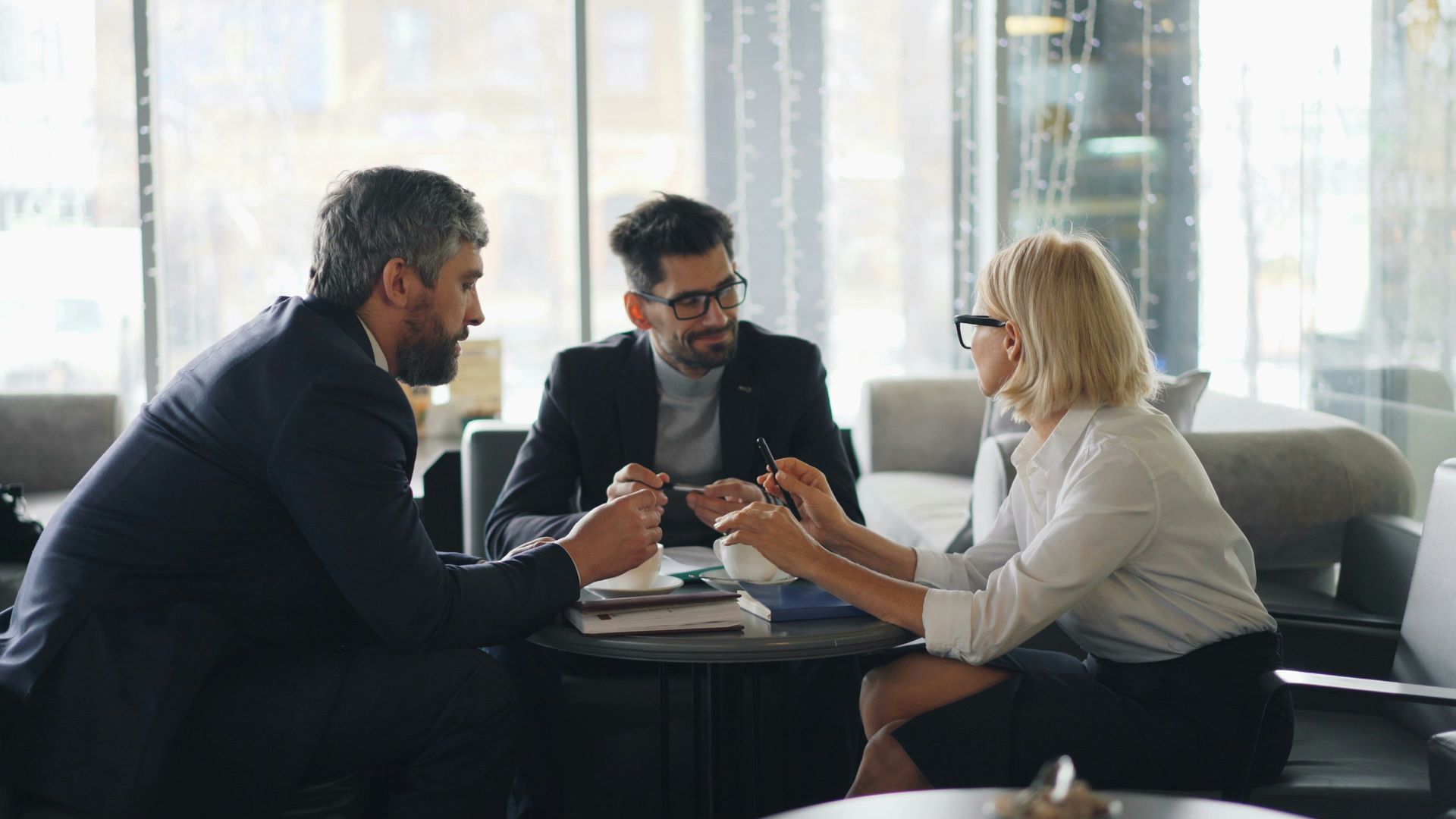 Three businesspeople in a meeting, around a table, inside a modern office space, discussing documents.